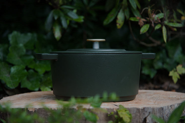 Donkergroene Dutch oven op een boomstronk in een groene, natuurlijke omgeving.